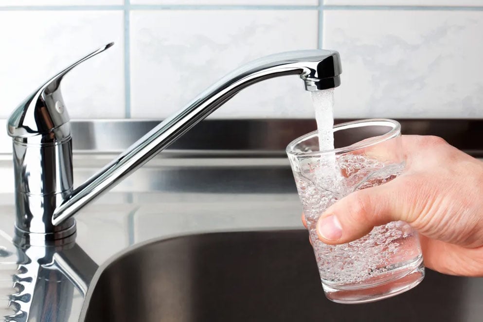 a person filling water in a glass from a tap