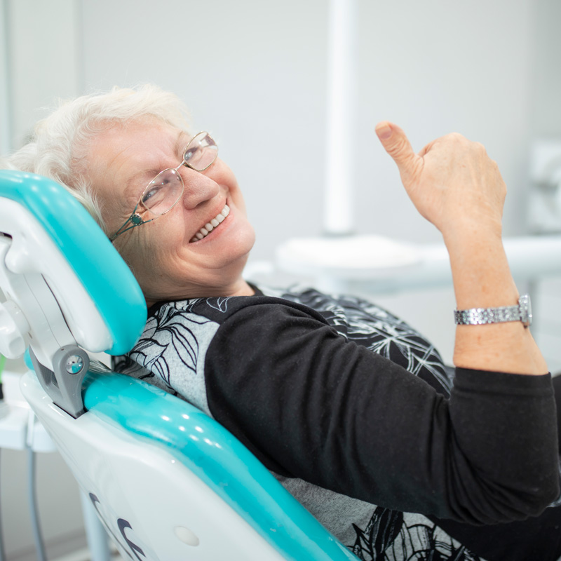 lady smiling in dental chair with thumbs up